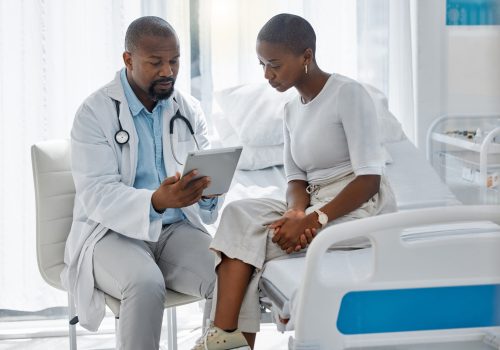 Doctor consulting patient with digital tablet, discussing diagnosis and medical checkup in hospital. Healthcare worker and trusted physician in appointment with medicine advice, wellness and feedback.